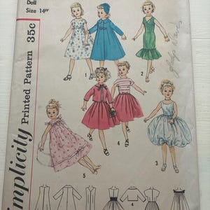 May include: A Simplicity printed pattern envelope for a 14 inch doll, number 2745. The front features illustrations of five dolls wearing various outfits including dresses, a coat, and a skirt set, with corresponding line drawings at the bottom.