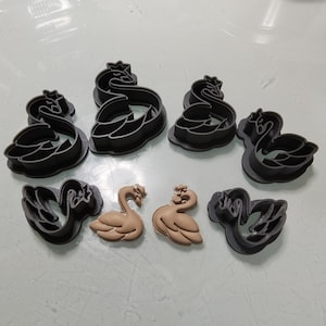 May include: Set of seven swan-shaped cookie cutters, including two smaller brown cutters and five larger black cutters. The cutters are made of plastic and are designed for making cookies or fondant decorations.
