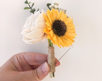 May include: A small bouquet of artificial flowers, featuring a yellow sunflower and a white rose, tied with twine and a pearl-headed pin.