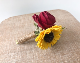 May include: A small bouquet of artificial flowers, featuring a red rose and a yellow sunflower, tied together with twine.