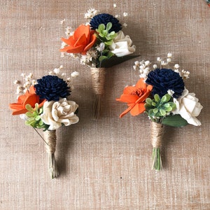 May include: Three small bouquets of artificial flowers, each tied with twine. The bouquets feature orange, white, and dark blue flowers.