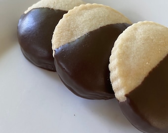 May include: Three round cookies with a half-circle of dark chocolate on top. The cookies are arranged in a row on a white plate.