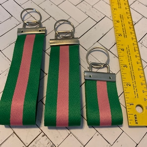 May include: Three green and pink striped keychains with silver key rings. The keychains are different sizes.