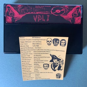 May include: A black cassette tape with a red and black Halloween-themed design. The tape is labeled "Vol. 1" and features a list of songs with titles like "Dracula's Daughter", "Monster Hop", and "Halloween Dance".
