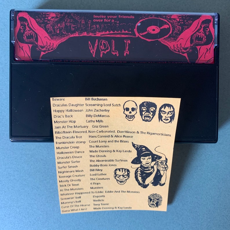 May include: A black cassette tape with a red and black Halloween-themed design. The tape is labeled "Vol. 1" and features a list of songs with titles like "Dracula's Daughter", "Monster Hop", and "Halloween Dance".