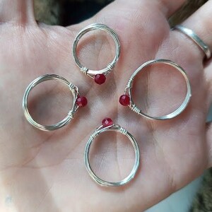 May include: Four silver wire rings with red gemstone accents. Each ring has a simple, circular design.