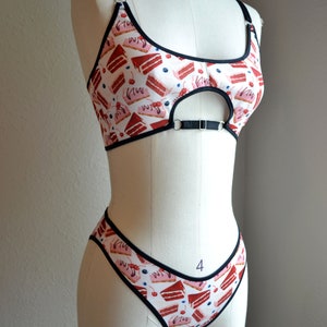 May include: A red and white lingerie set with a cake print. The bra has a keyhole cutout and adjustable straps. The matching underwear has a high-cut leg.