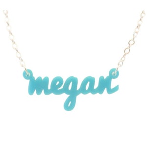 May include: A turquoise name necklace with the name "megan" in a cursive font. The pendant is suspended from a delicate silver chain. The necklace is a personalized jewelry item.