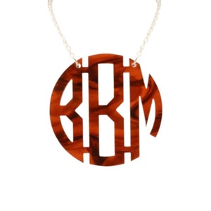 May include: A brown and white marbled circle pendant necklace with a cut-out monogram of the letters "BKM".