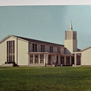 May include: A white building with a spire, surrounded by green grass. The building has a large window on the left side and several smaller windows on the right side.