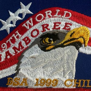 May include: Embroidered patch with a red border, featuring a blue background with white stars and a red and white striped design. The patch displays an eagle and the text "19TH WORLD JAMBOREE ESA 1999 CHILE".