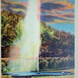 May include: A vintage postcard depicting a geyser erupting in a wooded area. The sky is a vibrant blue with pink and orange clouds. The text on the postcard reads "N649 - ANDREWS GEYSER AT ROUND KNOB ON SOUTHERN RAILWAY, WESTERN NORTH CAROLINA 45501".