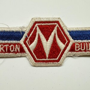 May include: A rectangular embroidered patch with a central hexagon featuring a white letter M on a red background. The horizontal bars are blue and red with the white text MORTON on the left and BUILDINGS on the right, all bordered in white.