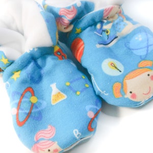 May include: A pair of blue baby booties with a white fleece lining. The booties feature a colorful pattern of cartoon girls, stars, planets, and science-themed objects.