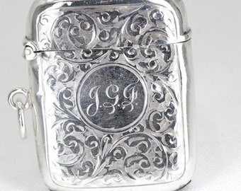 Könnte beinhalten: Ein silbernes Streichholzsafe mit einem gravierten Blumenmuster und den Initialen "J.G." in einem Kreis.