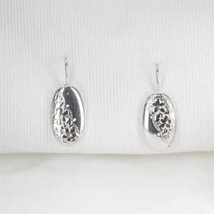 May include: A pair of silver earrings with a floral design. The earrings are oval shaped and have a delicate floral pattern.