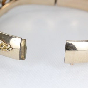 Puede incluir: Un brazalete de bisagra dorado con un dise&ntilde;o decorativo. El brazalete est&aacute; abierto y la bisagra es visible.