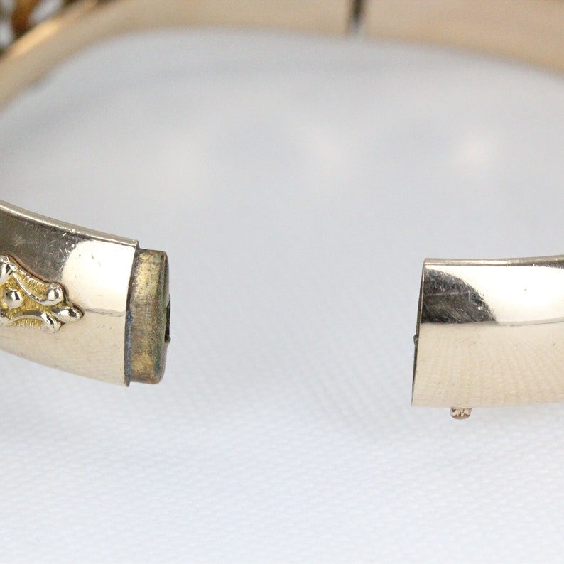 Puede incluir: Un brazalete de bisagra dorado con un dise&ntilde;o decorativo. El brazalete est&aacute; abierto y la bisagra es visible.