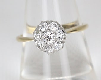 Op de afbeelding: Een gouden ring met een cluster van kleine diamanten die in de vorm van een bloem zijn gezet.