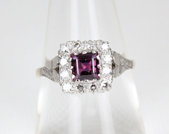 May include: A silver ring with a square-shaped purple gemstone surrounded by a halo of smaller white gemstones.