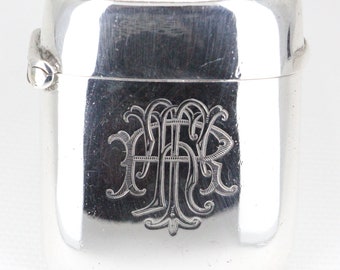 Könnte beinhalten: Silbernes Streichholzsafe mit einem gravierten Monogramm. Das Monogramm ist ein stilisiertes "M" mit einem dekorativen Schwung.
