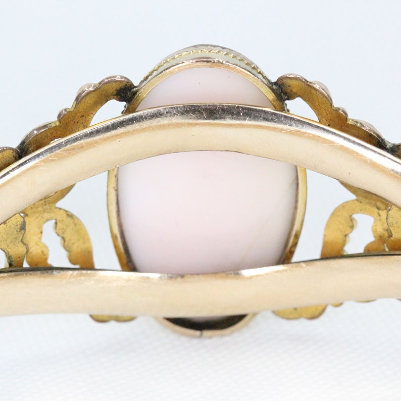 Puede incluir: Un anillo de oro con un delicado dise&ntilde;o de filigrana y un camafeo rosa en el centro.