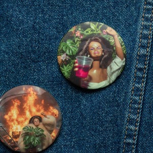 May include: A collection of five round buttons with various images, including a woman with a drink, a doll, and a woman in front of a fire. One button has the text "Common Houseplant Apparel". The buttons are displayed on a blue denim background.