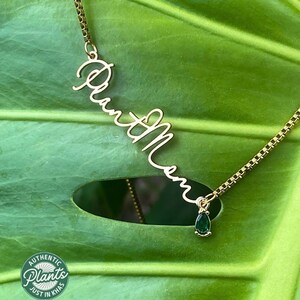 May include: Gold necklace featuring a cursive name pendant reading "Plant Mom" and a small green gemstone charm.