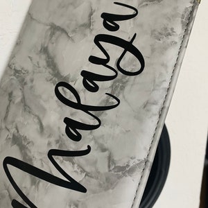 May include: A gray faux leather wallet with a marble pattern and the name "Malaya" written in black cursive.