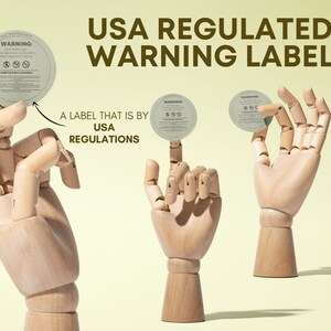 May include: Three wooden hands holding round, white warning labels with black text. The text on the labels reads "WARNING: Burn with Light Supervision. Keep Away From Children. Candle Specific Instructions". The text on the background reads "USA REGULATED WARNING LABEL" and "A LABEL THAT IS BY USA REGULATIONS".
