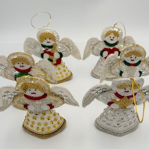 Peut inclure: Six décorations d'anges en perles blanches avec des halos en fil d'or. Chaque ange porte une robe de couleur différente et tient un instrument de musique.