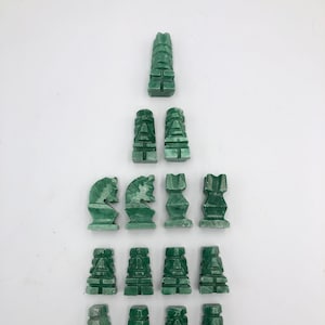 May include: A set of green jade chess pieces. The pieces are carved in a stylized design and are arranged in a pyramid shape.