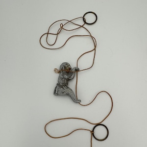 May include: A brown string with two metal rings and a small grey figurine of a monkey climbing the string.