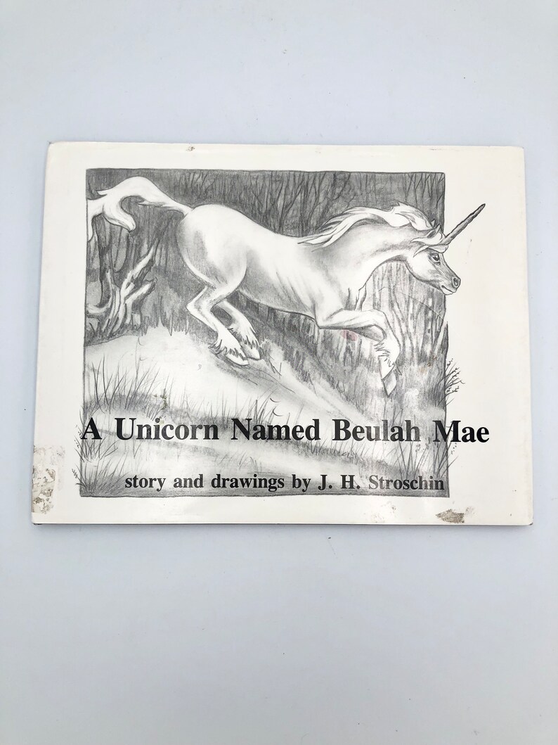 May include: A black and white illustration of a unicorn running through a forest. The title of the book is "A Unicorn Named Beulah Mae" and the author is J. H. Stroschin.