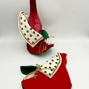 Puede incluir: Dos porta botellas de vino de fieltro rojo con detalles en fieltro verde y cuellos de fieltro blanco decorados con lentejuelas verdes. Los cuellos tienen ribetes dorados.