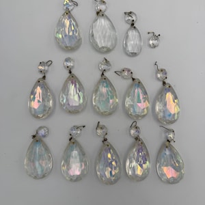 May include: A collection of fourteen clear, teardrop-shaped glass chandelier crystals with iridescent finishes. Each piece features a faceted surface and a small circular top bead, connected by a thin metal wire loop for hanging purposes.