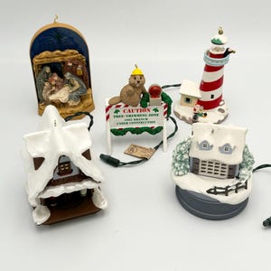 May include: A selection of Christmas ornaments, including a nativity scene, a lighthouse, a snow-covered house, and a beaver holding a sign. The sign reads "CAUTION TREE-TRIMMING ZONE 1992 BRANCH UNDER CONSTRUCTION."