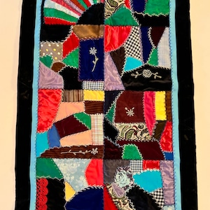 May include: A colorful patchwork quilt with a variety of fabrics and textures. The quilt is made up of many different shapes and sizes, and it is sewn together with a variety of stitches. The quilt is framed with a black velvet border and a light blue trim.