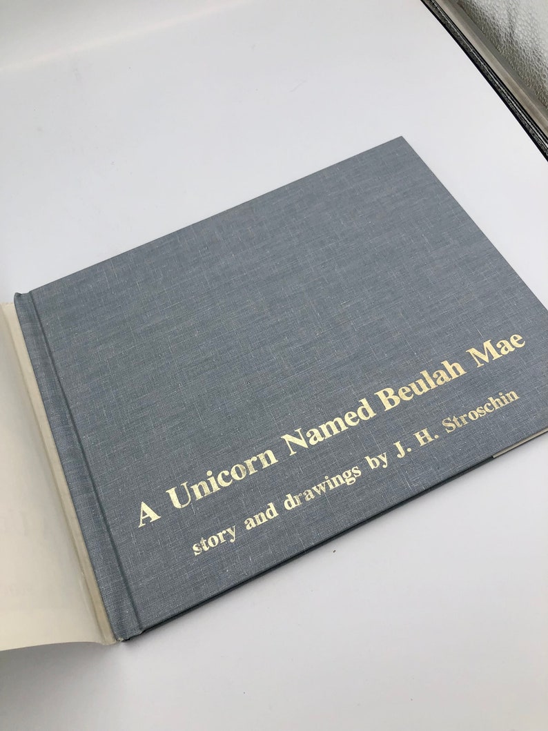 May include: A blue book with gold lettering on the cover. The title is "A Unicorn Named Beulah Mae" with the text "story and drawings by J. H. Stroschin" underneath.