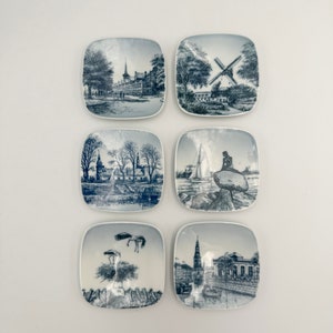 Può includere: Sei piccoli piatti quadrati in ceramica con illustrazioni blu e bianche di città e monumenti europei. I piatti sono disposti in due file di tre.