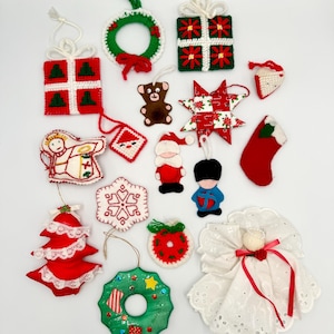 Op de afbeelding: Een verzameling van 15 handgemaakte kerstversieringen. De versieringen zijn gemaakt van vilt, stof en garen. Ze hebben verschillende ontwerpen, waaronder een kerstboom, een sok, een ster, een krans, een cadeau, een sneeuwpop, een kerstman, een engel en een teddybeer.