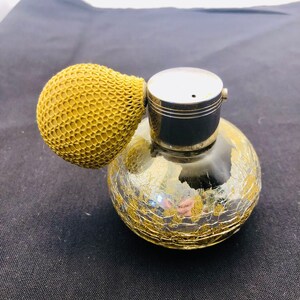 May include: A vintage glass atomizer with a gold-leaf design and a yellow rubber bulb. The atomizer has a silver top with a small hole for spraying.