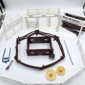 May include: A vintage Roy Rogers Double R Bar Ranch playset with a white wooden barn, brown wooden fences, a log cabin, and two yellow wagon wheels.