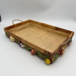 May include: A rectangular woven tray with a rope handle and a decorative floral trim. The trim is made of dried flowers and leaves in shades of pink, yellow, green, and purple.