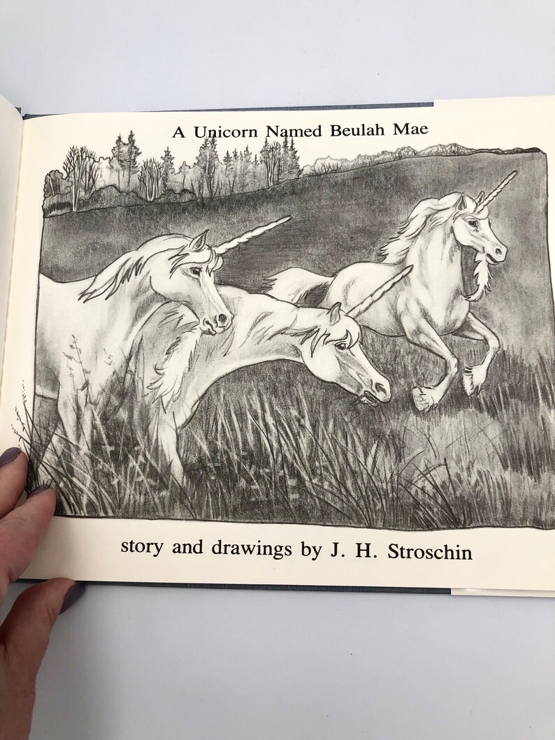 May include: A black and white illustration of three unicorns running through a field of grass. The text "A Unicorn Named Beulah Mae" is at the top of the image and the text "story and drawings by J. H. Stroschin" is at the bottom of the image.