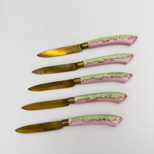 May include: Set of five antique butter knives with pink and green porcelain handles and gold accents.