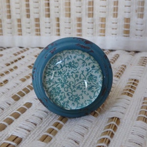 Puede incluir: Un pomo de armario redondo, de color turquesa, con un acabado envejecido. El pomo presenta un inserto de vidrio con un estampado floral turquesa y blanco. El pomo mide aproximadamente 3,8 cm de diámetro.