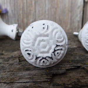 May include: Three white ceramic cabinet knobs with a black and white floral design. The knobs have a distressed finish and are perfect for adding a touch of farmhouse charm to any room.