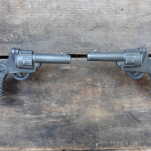 May include: Two black metal toy pistols with a star on the handle. The pistols are pointed in opposite directions.