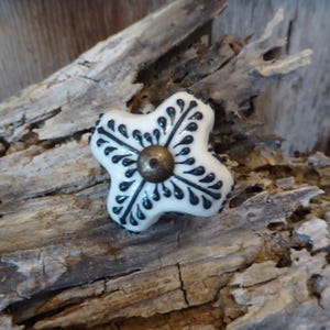 May include: White ceramic cabinet knob with a black and white floral design. The knob has a brass center.